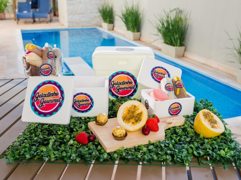 geladinhos gourmet de vários sabores com algumas frutas como maracujá, morango,bombom ferrero rocher e ao fundo uma piscina