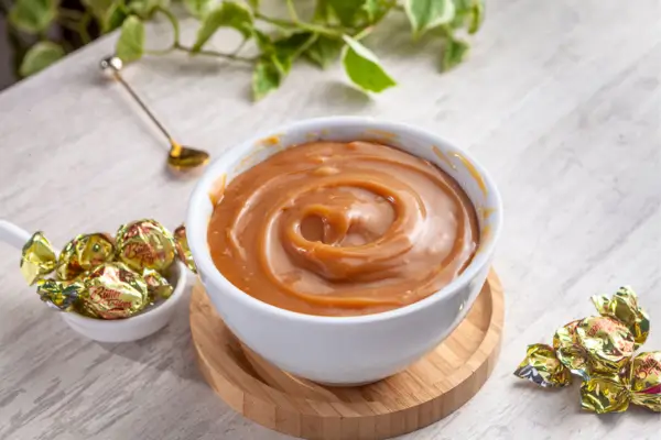 recheio firme de doce de leite para bolo em um bol branco e algumas balas de doce de leite em volta