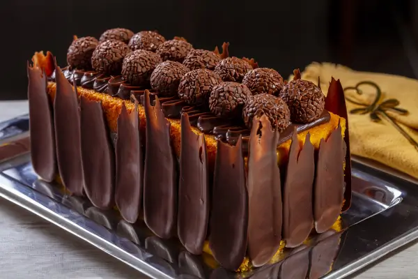 bolo quadrado de cenoura com cobertura e raspas de chocolate e brigadeiros em cima