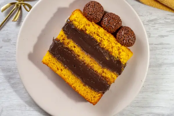 fatia de bolo de cenoura com recheios de chocolate com cobertura de chocolate e tres brigadeiros em cima